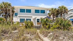 A coastal house with a sandy beach in front, palm trees, and a clear blue sky. - Beach House - Family Tides by PHG (Panama City Beach)