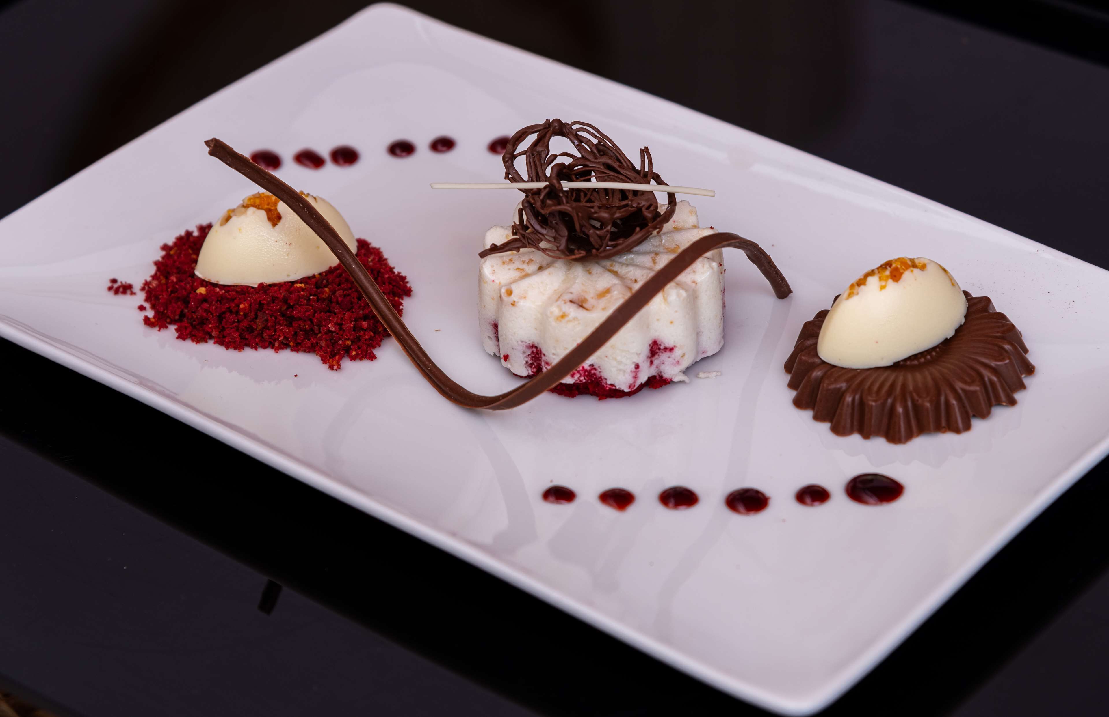 A dessert plate with three different desserts, each with unique garnishes and chocolate decorations.