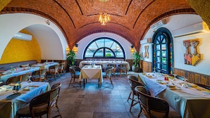 Een restaurant met bakstenen bogen, ronde tafels en rieten stoelen.