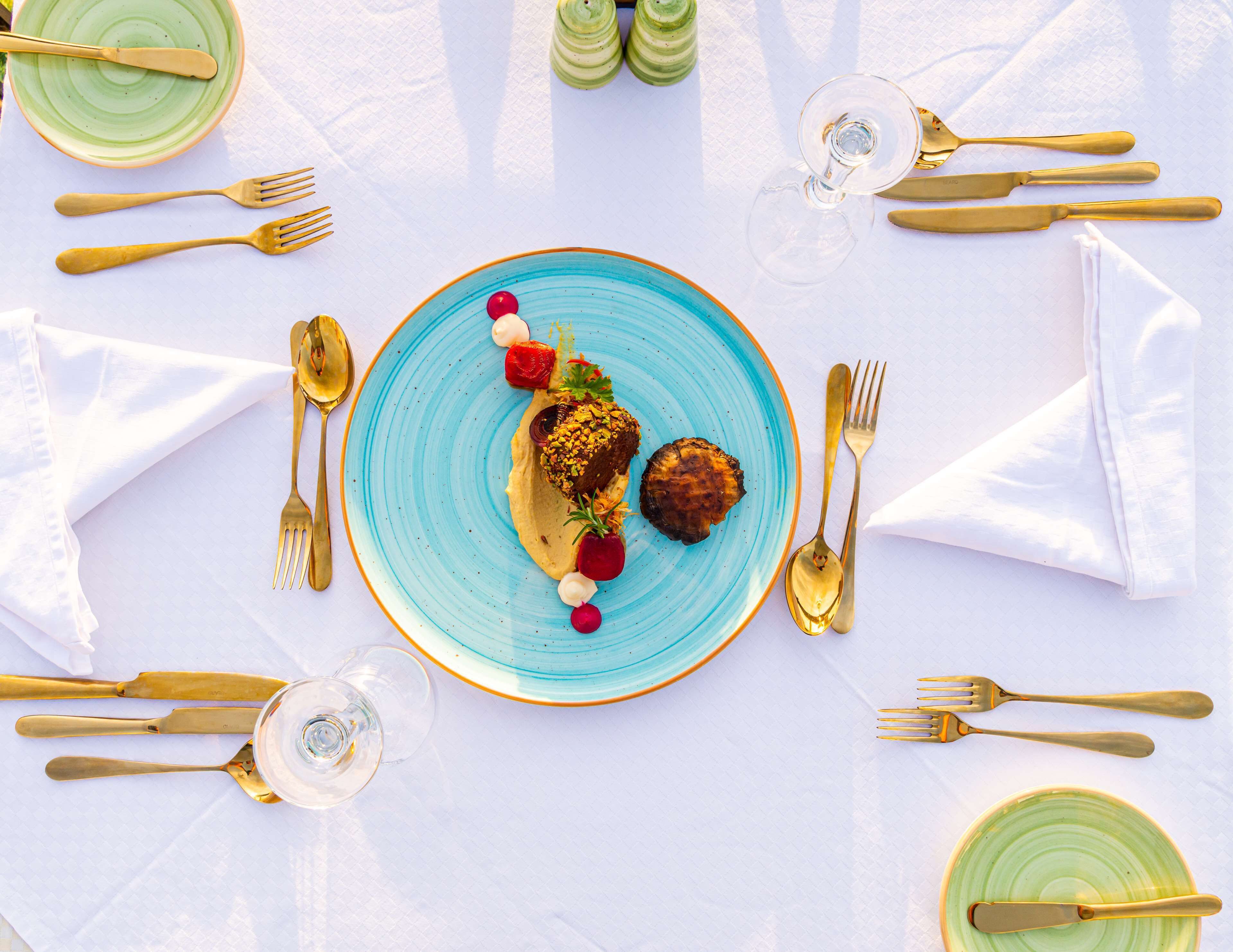 A table set with a blue plate, gold cutlery, and a glass of water.