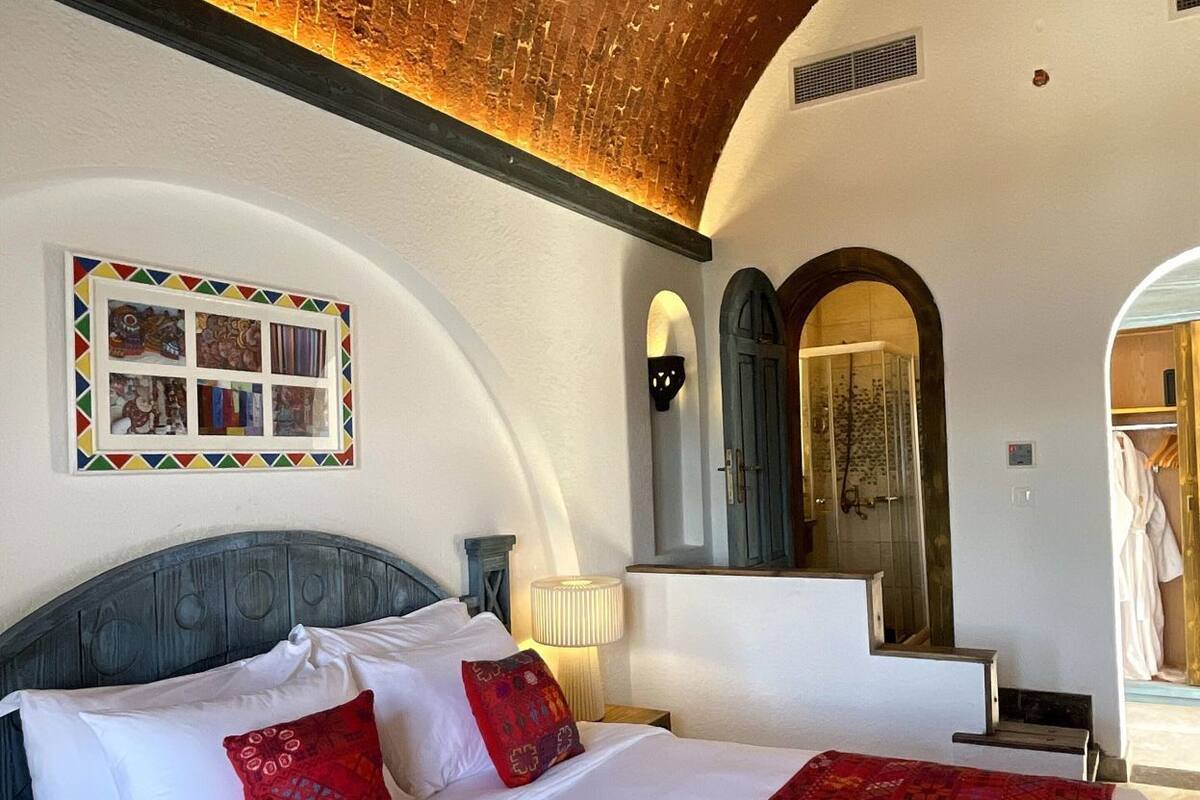 Ein Hotelzimmer mit Backsteinverkleidung, einem Bett mit weißer und roter Bettwäsche, einem gerahmten Bild an der Wand und einem Spiegel über dem Bett.