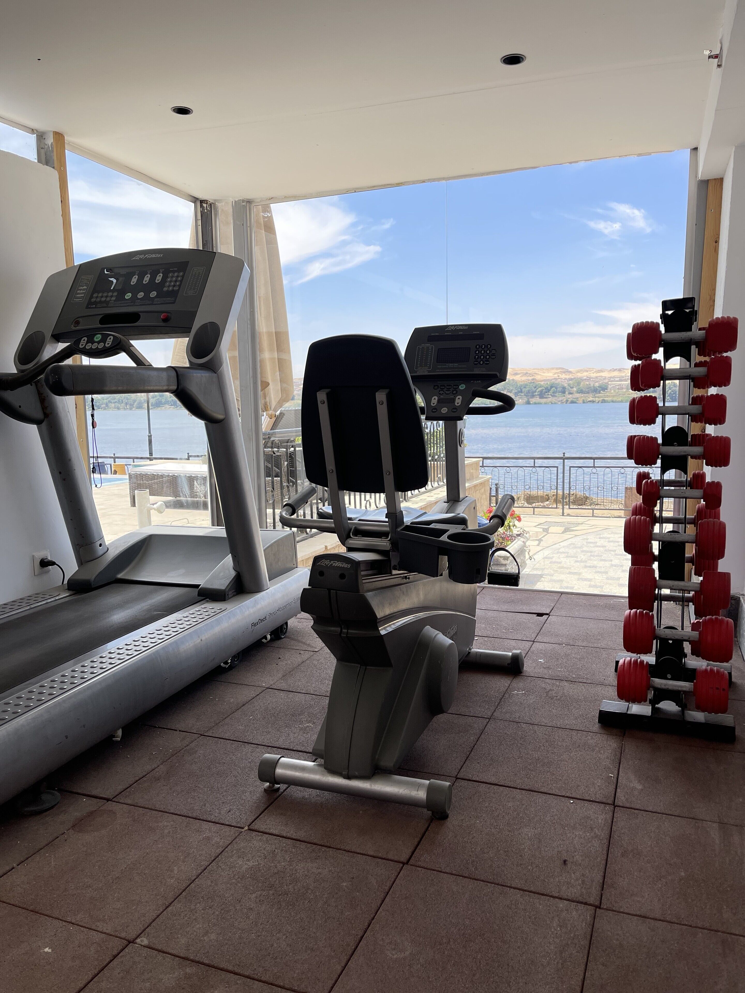 A gym with treadmills, a stationary bike, and a set of red dumbbells.