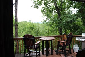 A deck with two Adirondack chairs and a small table, overlooking a forested area. - Mountain View’s, hot tub, and game room! (Sautee Nacoochee)