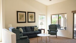 Een woonkamer met een donkergroene bank, een bijpassende fauteuil, een klein rond salontafeltje en twee ingelijste botanische prints aan de muur.
