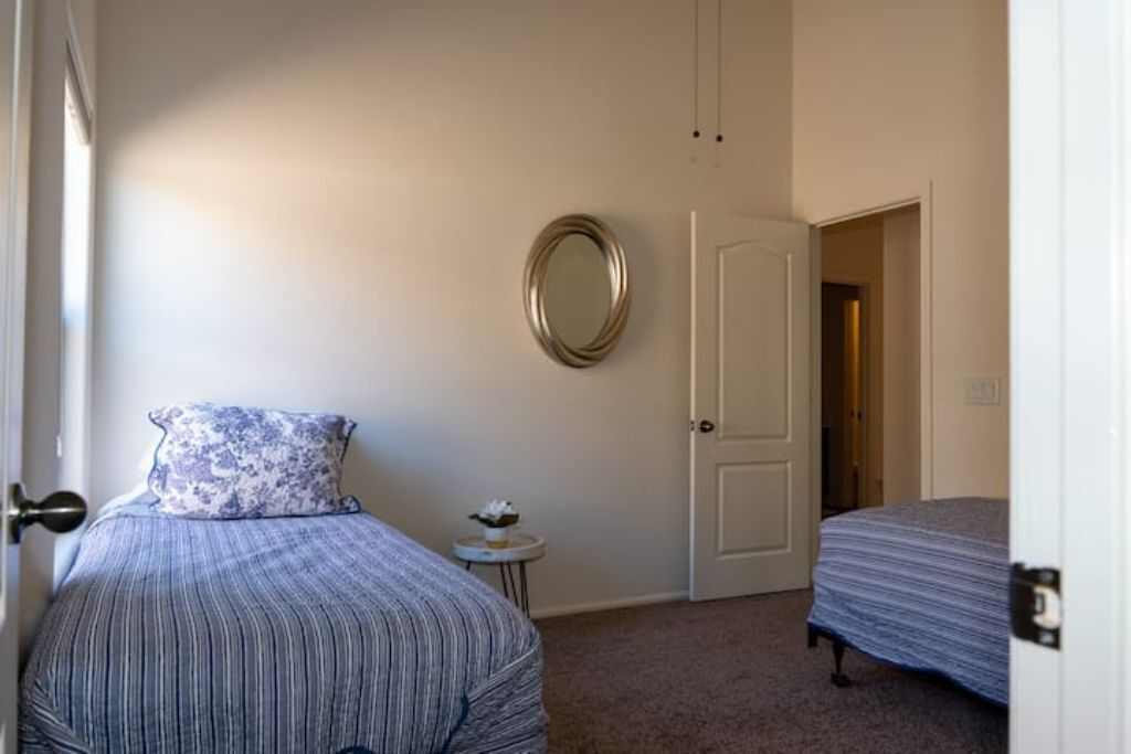 Een slaapkamer met een bed, een ronde spiegel en een deur.
