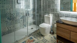 Ein Badezimmer mit Dusche, Toilette und Waschbecken, ausgestattet mit gemusterten Fliesen und einem Spiegel.