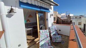 Eine Dachterrasse mit Essbereich, einem Sessel mit Blumenmuster und Blick auf benachbarte Gebäude.