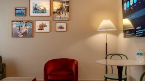 Ein Hotelzimmer mit einem roten Sessel, einem kleinen Tisch, einer Lampe und gerahmten Bildern an der Wand.