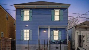 A two-story house with a blue exterior, a front porch, and a black metal fence. - Lux and Spacious for Groups near French Quarter (New Orleans)