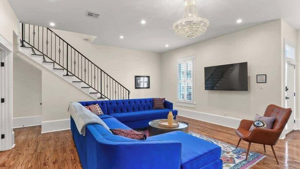 A living room with a blue sectional sofa, a coffee table, a brown leather armchair, a chandelier, and a staircase. - Lux and Spacious for Groups near French Quarter (New Orleans)