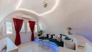 A modern, curved living area with a sofa, red curtains, and a small table. - Canyon Santorini (Fira)