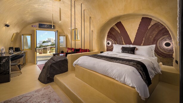 A bedroom with a bed, a desk, and a chair. There is a view of the outside through a window. - Canyon Santorini (Fira)