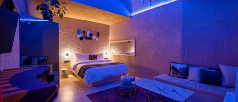 A modern bedroom with a bed, a sofa, a small table, and a mirror.