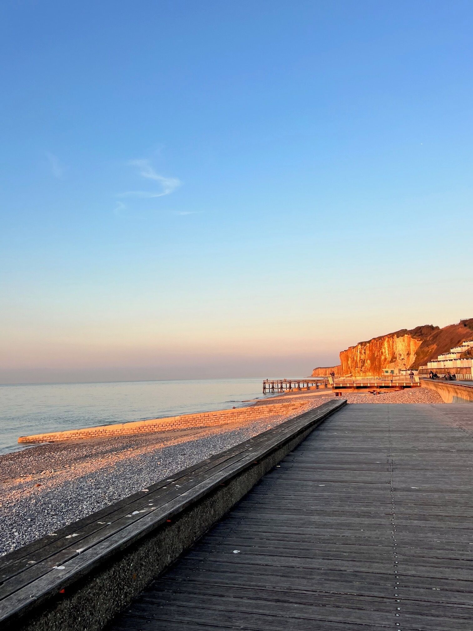 A wooden boardwalk leading to a beach with a rocky shoreline and a cliff in the background.
