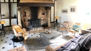 Una sala de estar acogedora con chimenea de ladrillo, vigas de madera y suelo a cuadros. Hay dos sillones, un sofá y una mesa de centro con objetos decorativos.