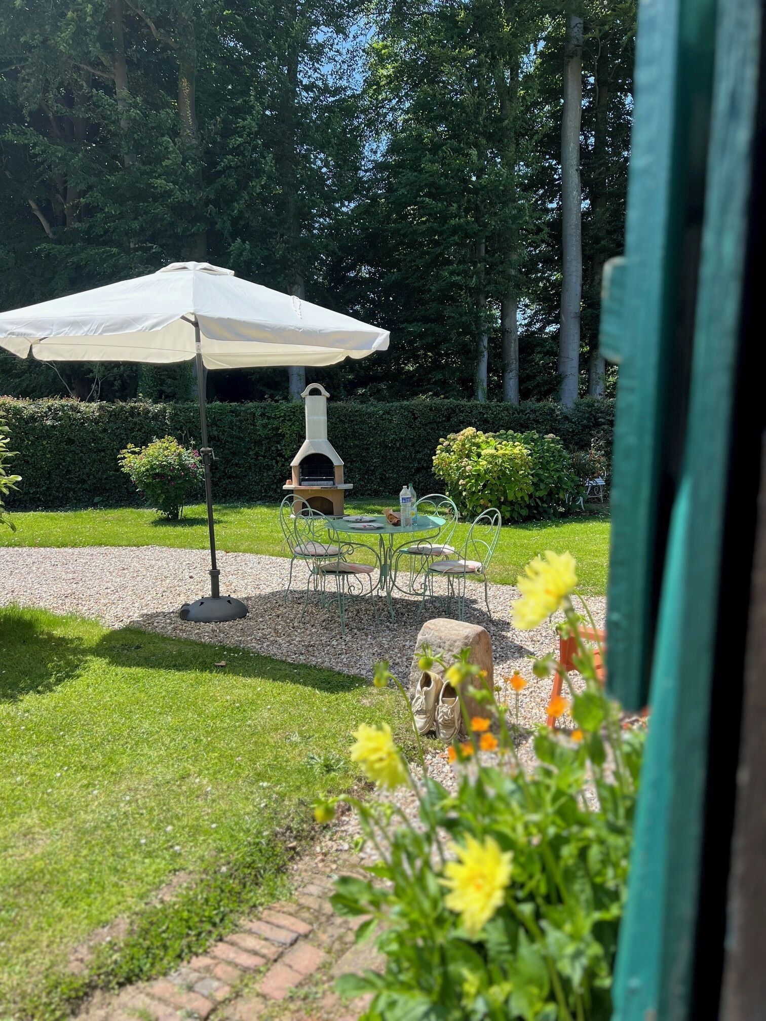 A garden patio with a pizza oven, outdoor table and chairs, and a white umbrella.