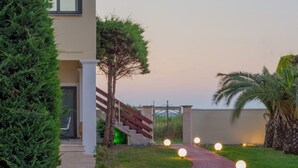A pathway leading to a building with a gated entrance, surrounded by greenery and palm trees.
