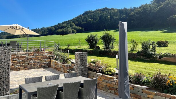 An outdoor patio with stone walls, wicker furniture, and a large umbrella. - Vacation apartment in Gerolstein, with a view of the Dolomites, up to 8 people (Gerolstein)