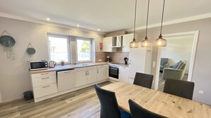 A modern kitchen with white cabinets, a wooden dining table, and black chairs. There are hanging pendant lights and a view into the living area. - Vacation apartment in Gerolstein, with a view of the Dolomites, up to 8 people (Gerolstein)
