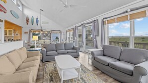 A spacious living room with grey sofas, a white coffee table, and a dining area with a wooden table and chairs. - Oceanfront Home in Waves with Pool, Hot Tub, and Game Room (Waves)