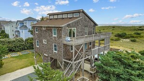 A two-story wooden house with a balcony and a sign indicating a surfboard rental service. - Oceanfront Home in Waves with Pool, Hot Tub, and Game Room (Waves)