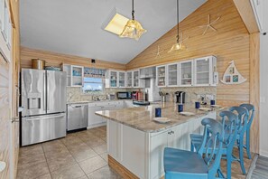 A modern kitchen with white cabinets, a central island, and blue bar stools.