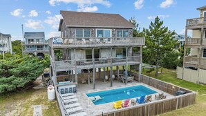 A two-story house with a pool, deck chairs, and a surfboard sign. - Oceanfront Home in Waves with Pool, Hot Tub, and Game Room (Waves)