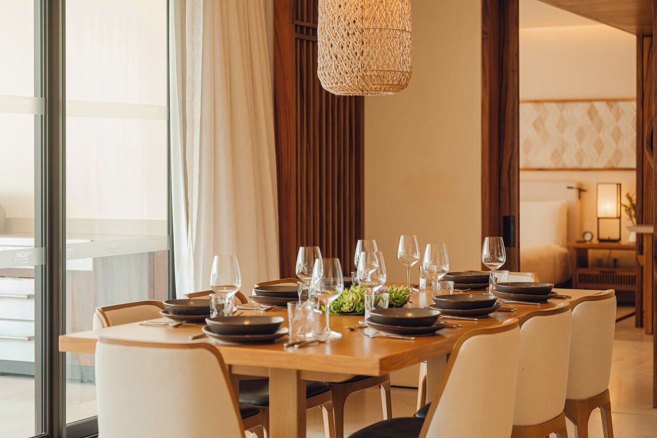 Uma sala de jantar com uma mesa redonda posta para seis pessoas, rodeada por cadeiras.