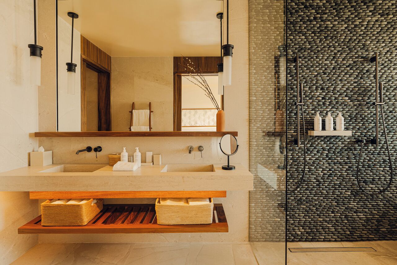 Een moderne badkamer met een grote spiegel, twee wastafels en een douchegedeelte met een stenen wand.