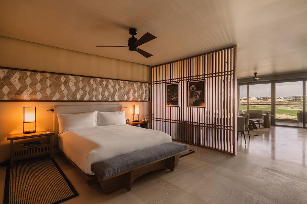 A modern hotel room with a large bed, bedside lamps, a ceiling fan, and a view of the outdoors.