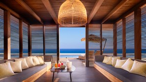 Una terraza de madera con vista al océano, amueblada con sofás y una mesa con bebidas.