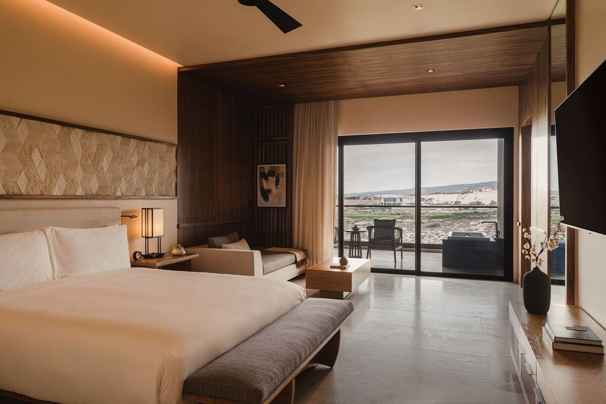 A modern hotel room with a large bed, a sofa, a desk, and a view of the beach.