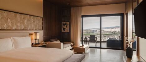 Habitación de hotel moderna con una cama grande, un sofá, un escritorio y vistas a la playa.