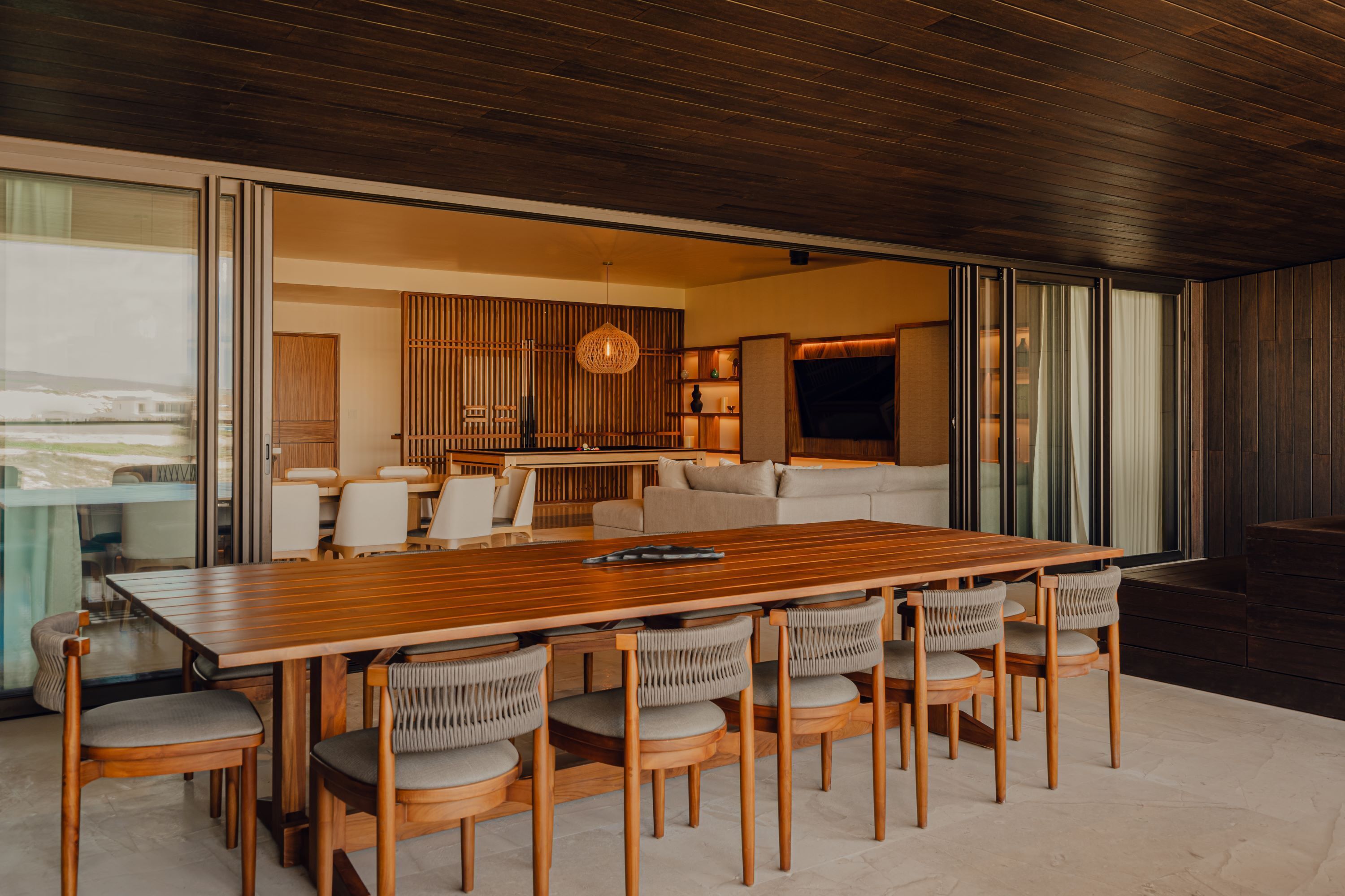 A modern dining area with a wooden table and chairs, a sofa, and a kitchen in the background.