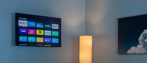 Habitación con televisión mostrando aplicaciones de transmisión, una mesa, sillas, una lámpara y un sofá.