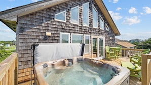 Une maison en bois avec un jacuzzi sur une terrasse en bois, entourée de chaises vertes.
