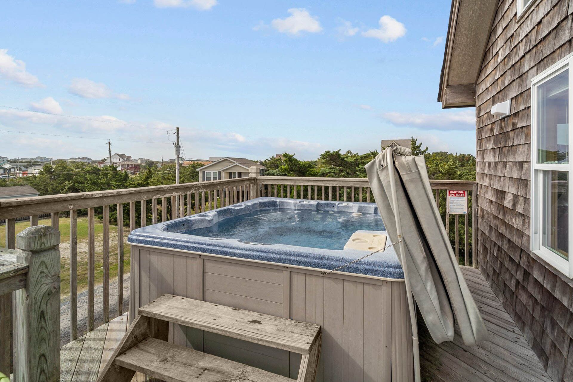 A hot tub on a wooden deck with a view of houses and trees in the background.