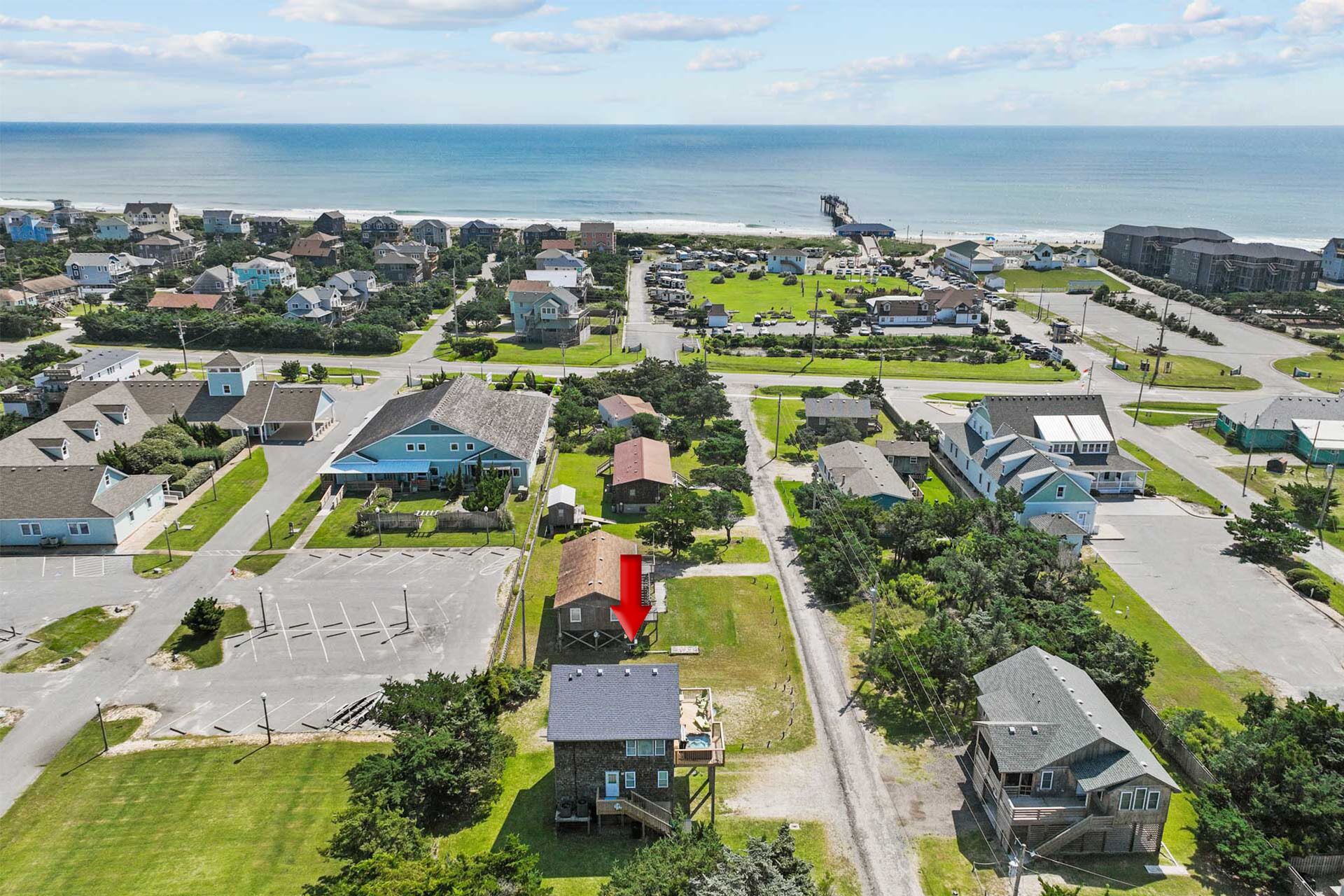 An aerial view of a coastal residential area with houses, a parking lot, and a pier extending into the sea.