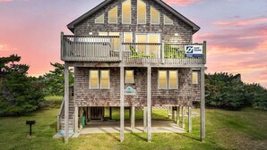Une maison en bois à deux étages, dotée d’un balcon, d’une enseigne indiquant « Surf Sound Real Estate » et d’une autre enseigne représentant « Salty Frog ».