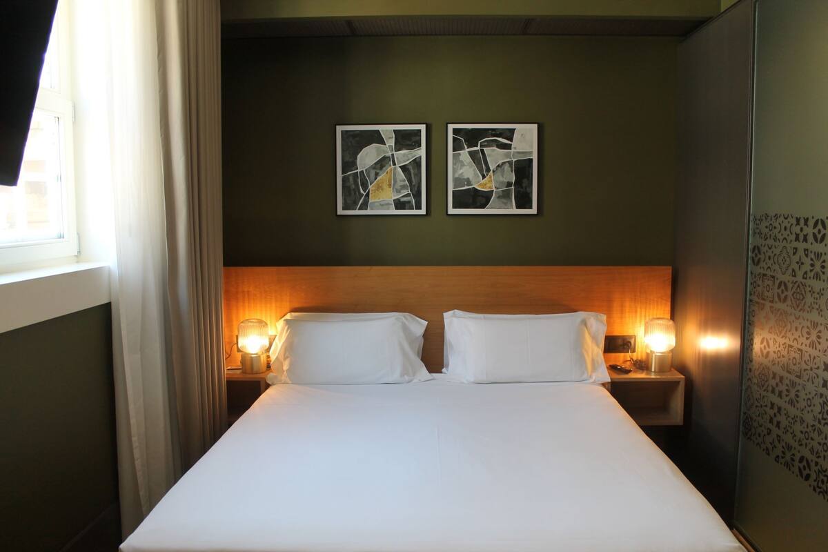 A hotel room with a large bed, two bedside lamps, and abstract artwork on the wall.