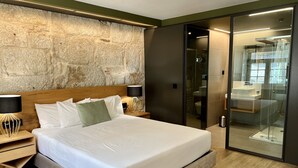 Een moderne hotelkamer met een groot bed, een accentmuur van steen, een badkamer met glazen wanden, en een houten vloer.