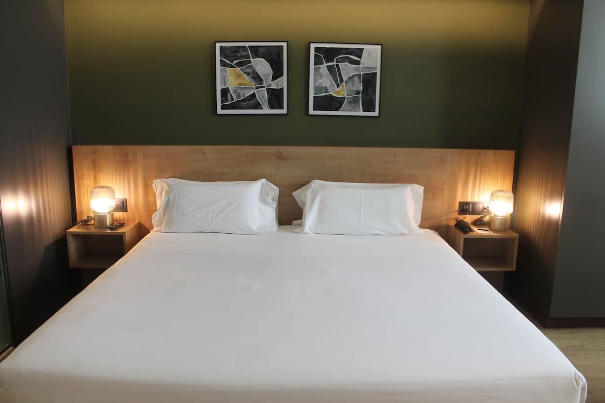 A hotel room with a large bed, two bedside tables with lamps, and abstract art on the wall.