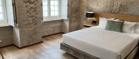 Ein Schlafzimmer mit Steinwand, einem Bett mit weißer Bettwäsche, einem Nachttisch mit Lampe und einem Fenster mit Blick.