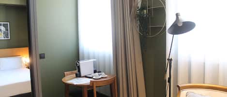 Quarto de hotel com cama, escrivaninha com laptop, cadeira, abajur e janela com cortinas.