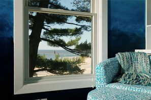 A room with a large window offering a view of a beach and a tree.