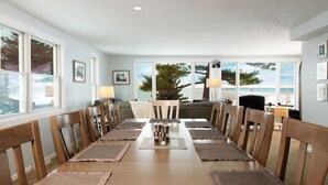 Una sala da pranzo con un tavolo lungo, sedie e vista sulla spiaggia attraverso ampie finestre.