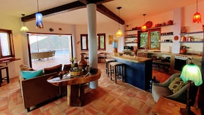 Un vaste espace de vie comprenant une cuisine et un coin repas, avec une grande fenêtre, une table en bois et un bar.