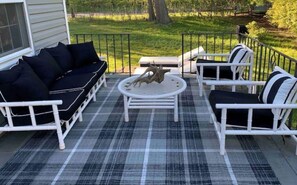 Relax on the patio with a sofa, coffee table, and armchairs, surrounded by a grassy view.