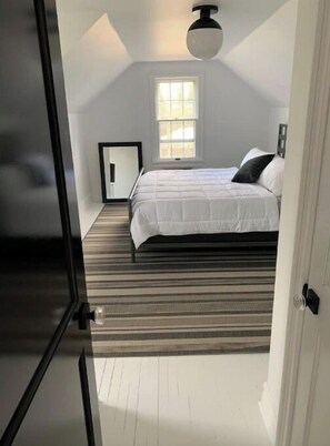 Cozy retreat with a large bed, window, and door, set against a sloped ceiling with a light fixture.