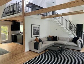 Relax in this spacious living area with a high ceiling and exposed beams, featuring a comfortable L-shaped sofa and a stylish coffee table.